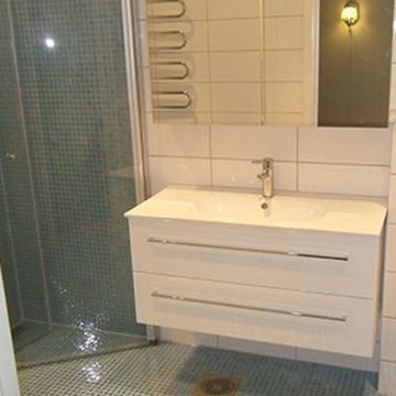 Baderom med turkis mosaikkflis på gulv og i dusj og hvitt servantskap med speil over